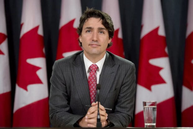 Canadian prime minister Justin Trudeau sits at a desk flanked by Canadian national flags.