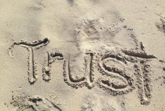 A photograph of the word trust written in the sand